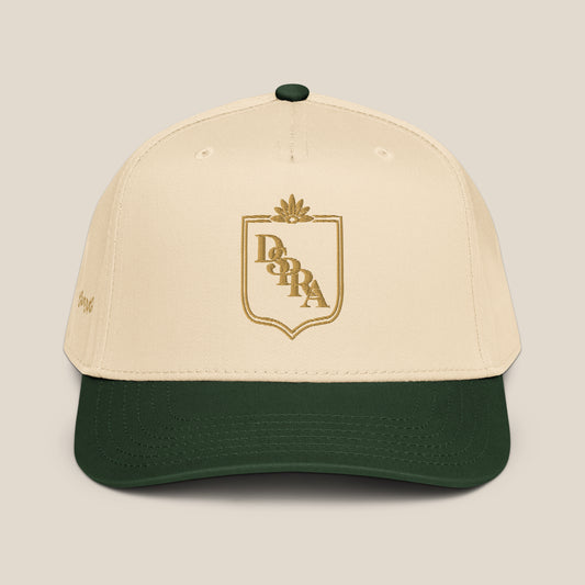 A baseball cap with an off-white crown and a dark green visor, featuring a gold embroidered crest with "DSPRA" (pronounced diaspora).